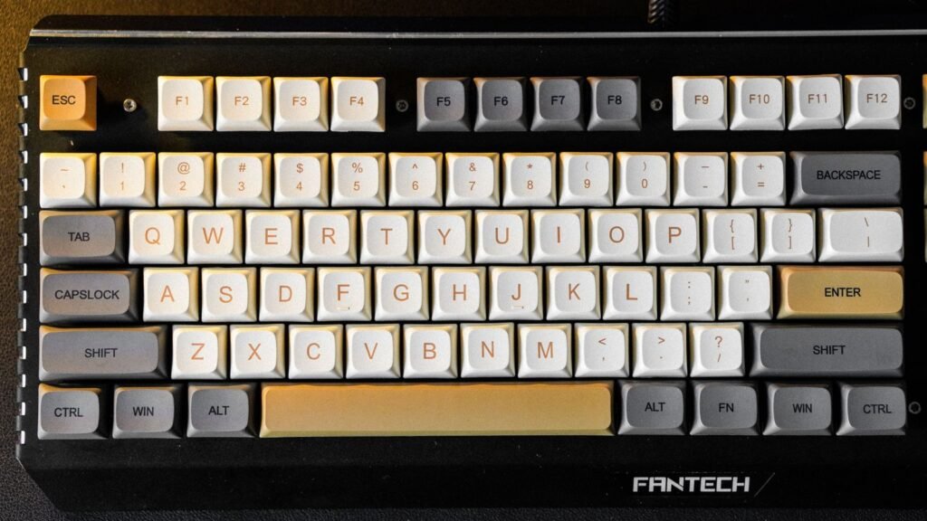 Top-down view of a black Fantech mechanical keyboard with cream, gray and orange keycaps and visible screws on the top plate