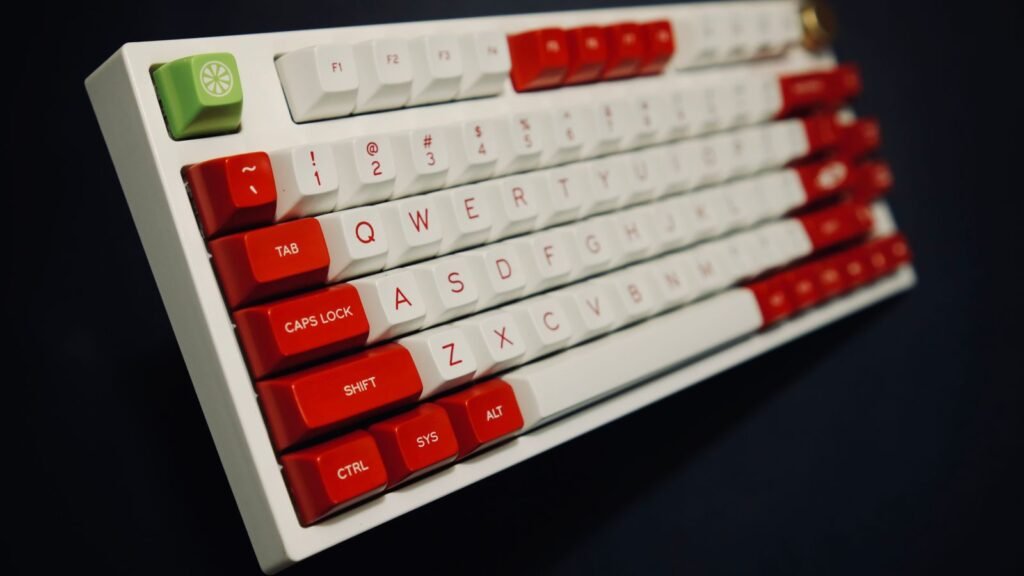 Compact mechanical keyboard with a white case, red and white keycaps and a green lime-print Escape key on a dark background