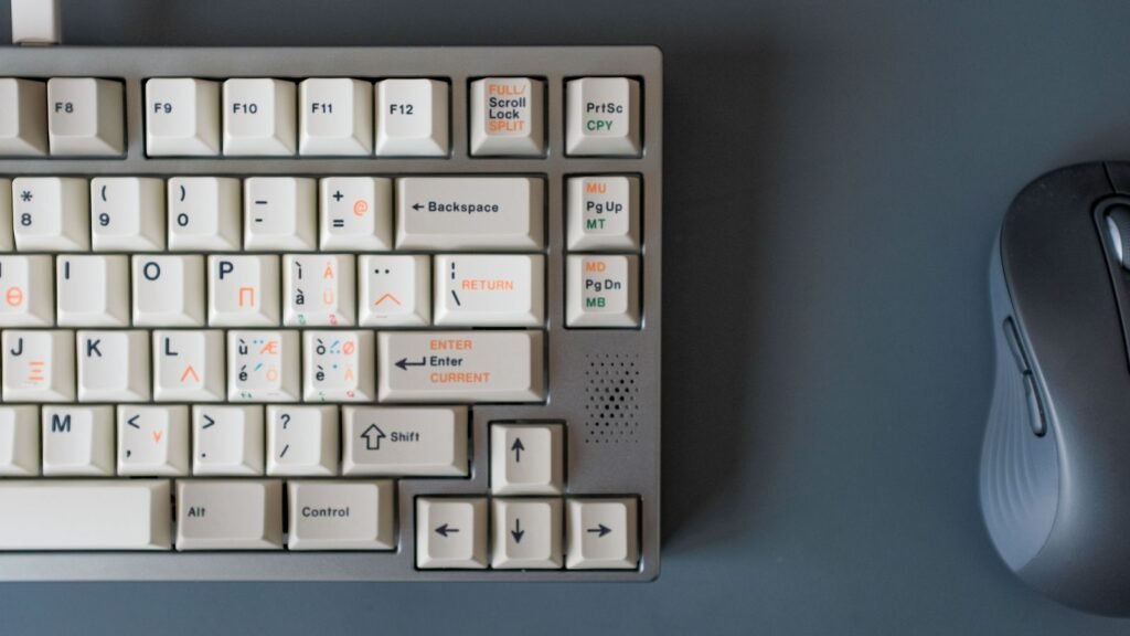Top-down view of the right side of a gray aluminum mechanical keyboard with cream keycaps next to a dark computer mouse