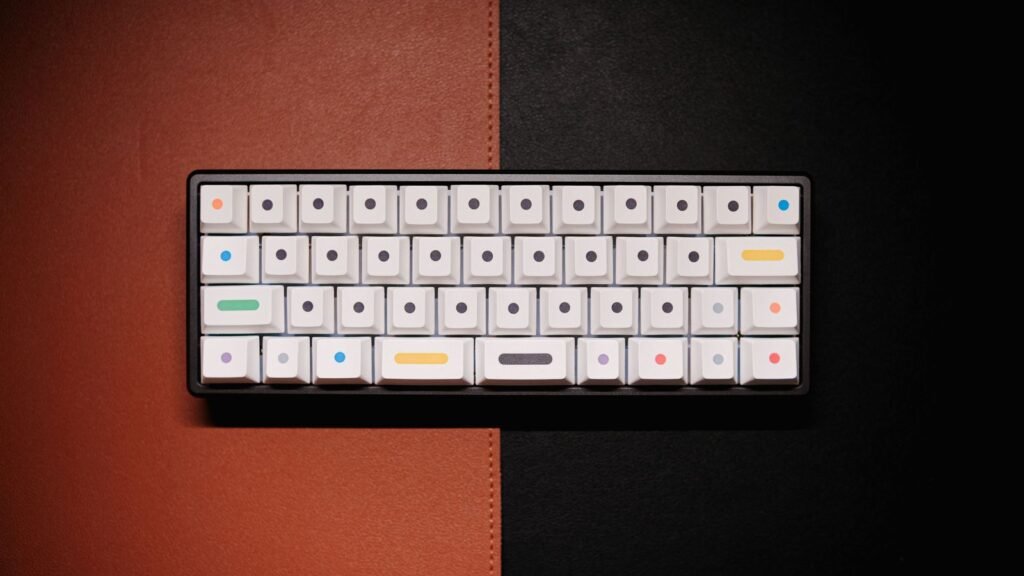 A tiny white keycap keyboard with colored dots on a dark gray case, lying on orange and black leather