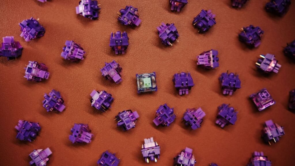 Dozens of loose purple mechanical keyboard switches scattered on a brown leather surface, with one clear switch in the center