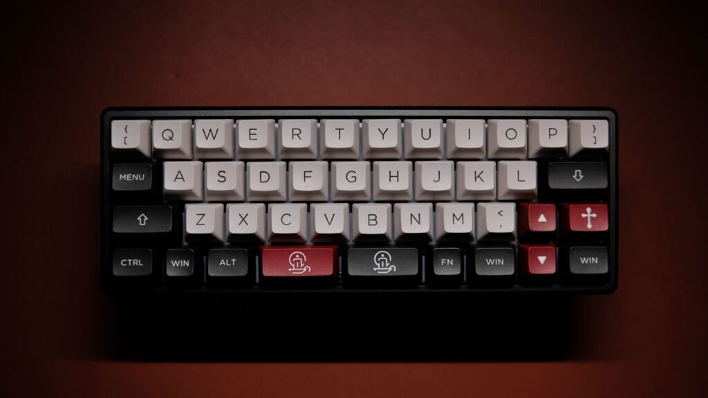 Overhead view of a very small 40 percent mechanical keyboard with gray and white keycaps, a split spacebar and no number row, on a dark red background