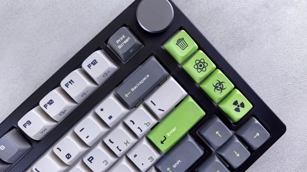 Close-up of the top right corner of a black mechanical keyboard with gray and white keycaps, green accent keys and a metal rotary knob