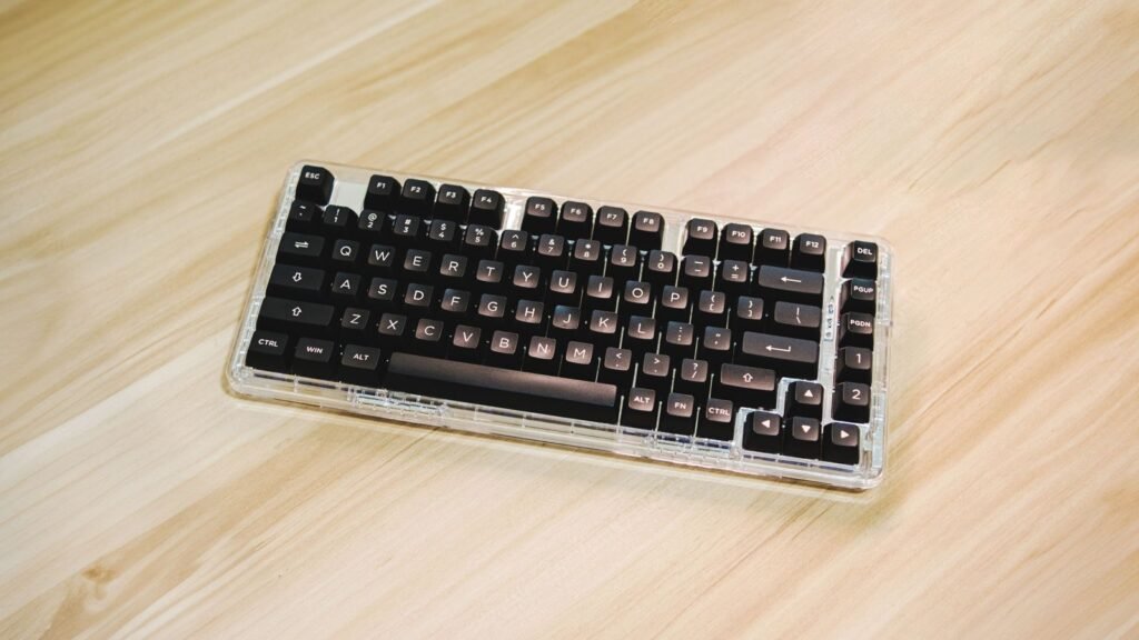 Compact mechanical keyboard with black keycaps in a clear transparent case on a light wooden desk