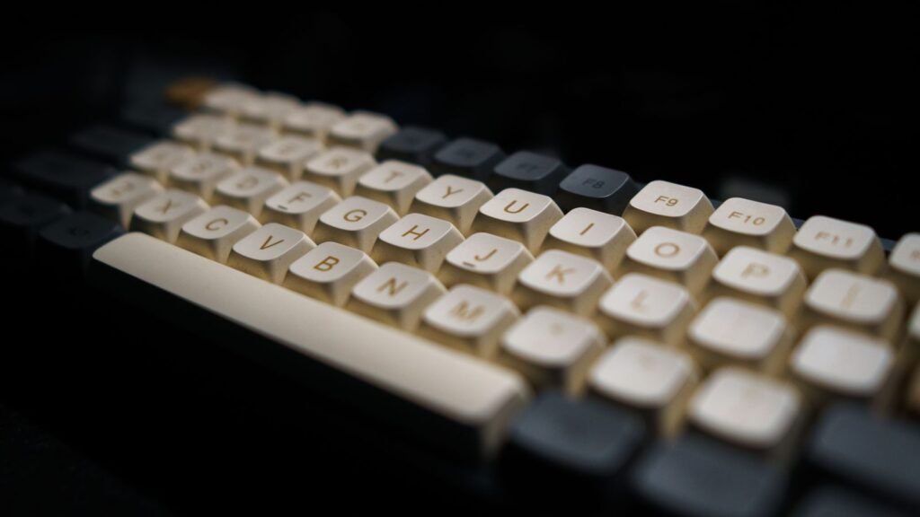 Close-up of a mechanical keyboard with cream keycaps and dark gray modifier keys in low light