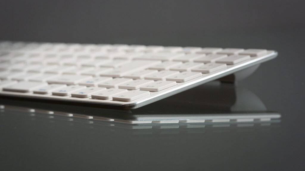 Close low-angle view of a thin white keyboard with flat keys on a reflective dark glass surface