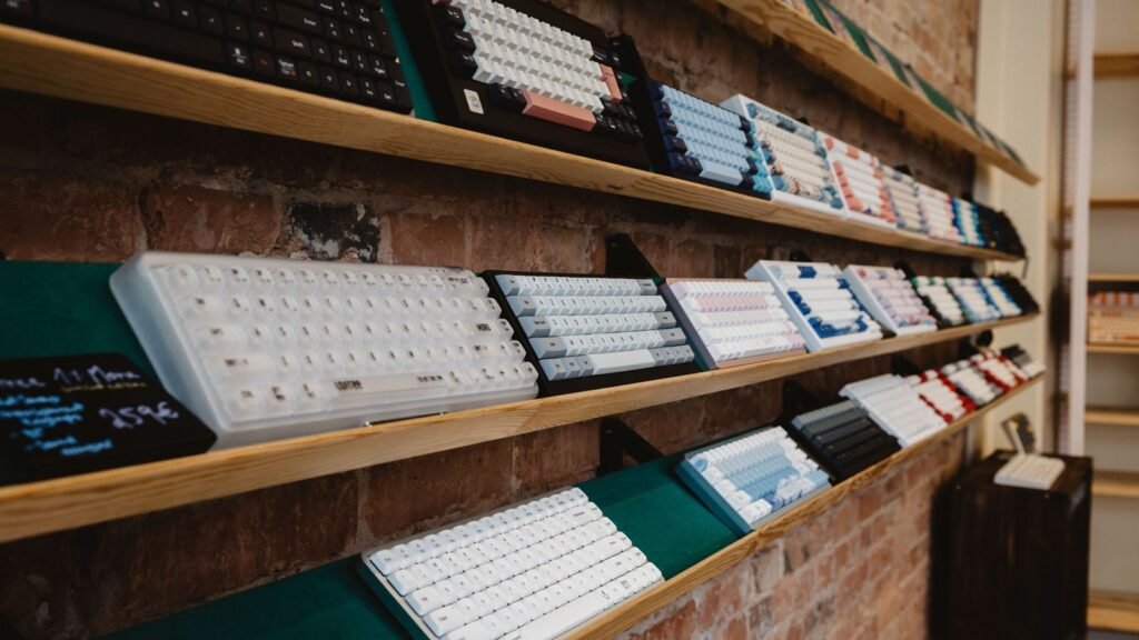 Rows of mechanical keyboards in different sizes and keycap colors displayed on wooden shelves against a brick wall