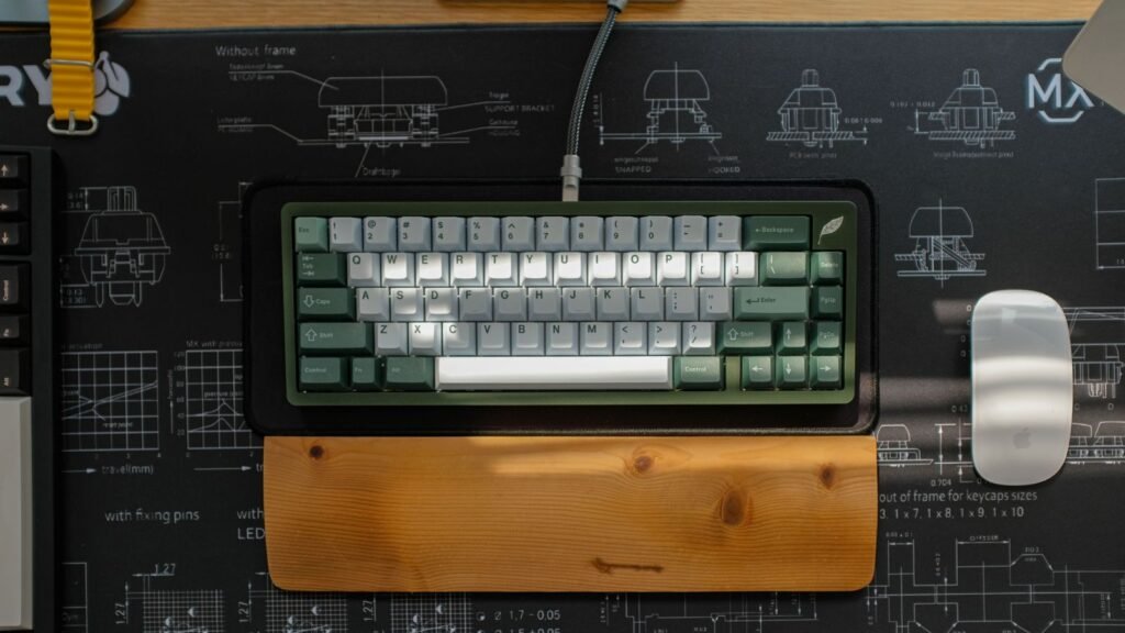 A green and white 65 percent mechanical keyboard on a dark desk mat with a wooden wrist rest in front of it