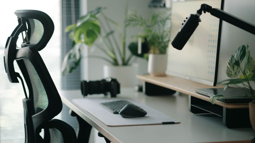 A black mesh office chair with a headrest beside a desk holding a low keyboard, mouse and raised monitor