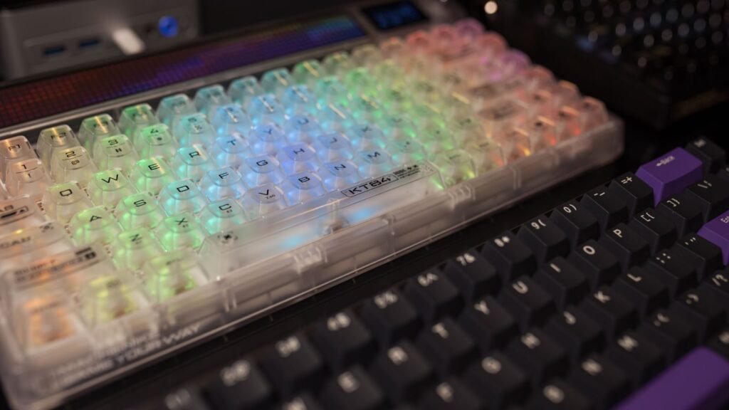 A mechanical keyboard with clear translucent keycaps glowing in rainbow RGB light, next to a black keyboard with purple accents