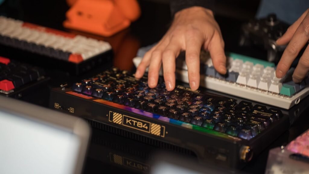 Hands typing on a dark mechanical keyboard with glossy keycaps, with other enthusiast keyboards around it