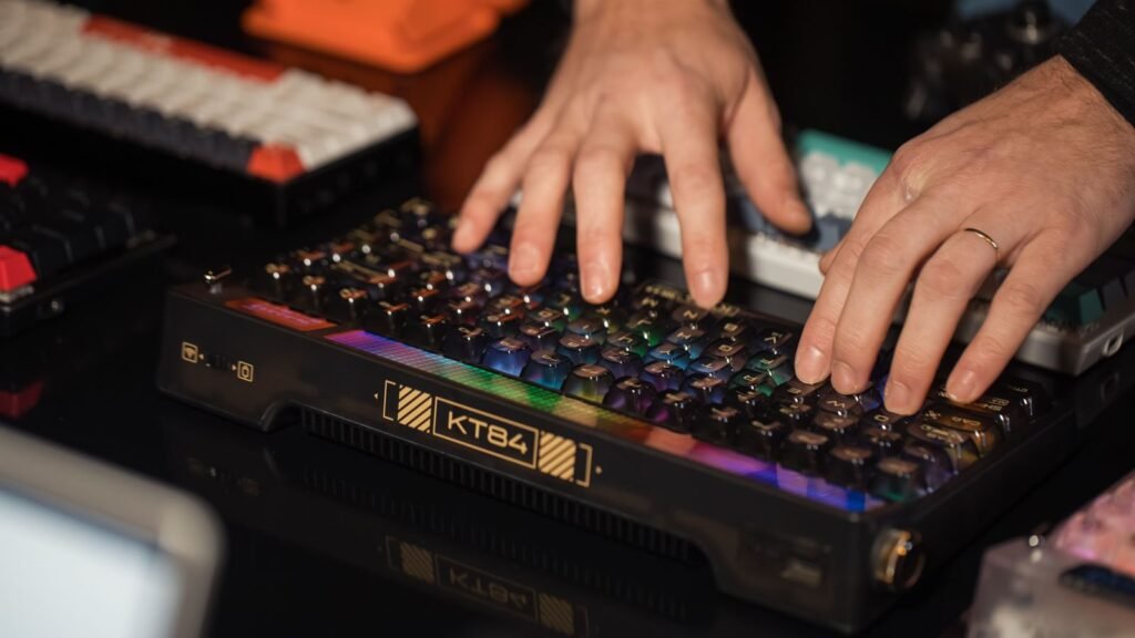 Hands typing on a black mechanical keyboard with glowing RGB keycaps, with other keyboards around it on a dark desk
