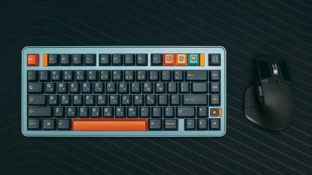 A compact mechanical keyboard with gray and orange keycaps and a black mouse on a dark striped desk mat