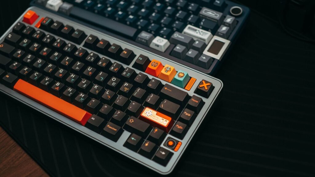 Two compact mechanical keyboards with knobs on a dark desk mat, the front one with a function row, a column of navigation keys and an arrow cluster