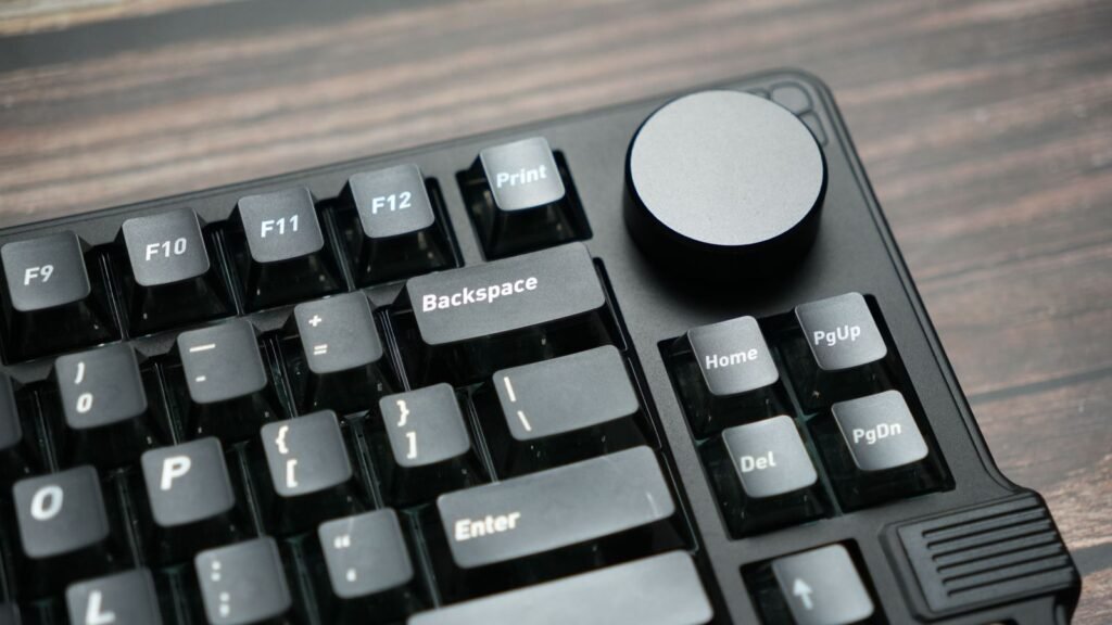 Close-up of a black mechanical keyboard with dark keycaps and a large round metal volume knob above the navigation keys