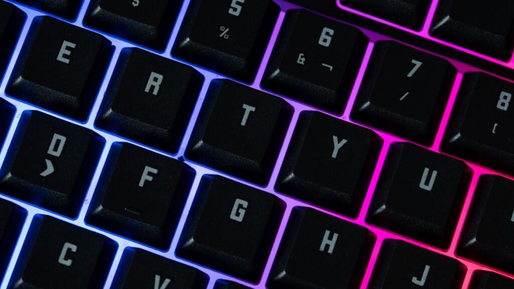 Close-up of black keycaps on a keyboard lit from underneath by blue, purple and pink RGB lighting