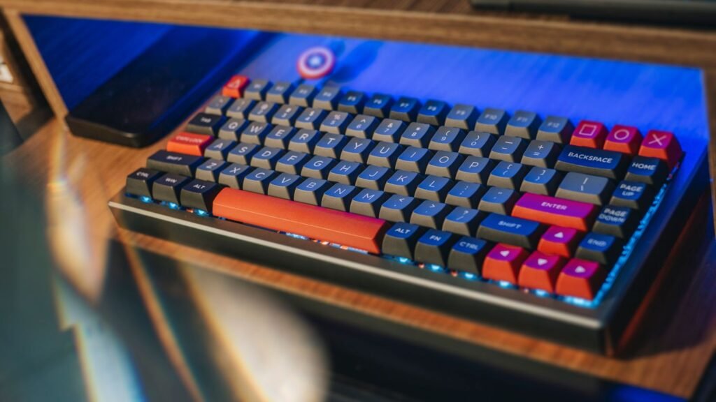 Compact mechanical keyboard with gray, blue and orange keycaps and a separate arrow cluster, sitting on a wooden desk under blue light