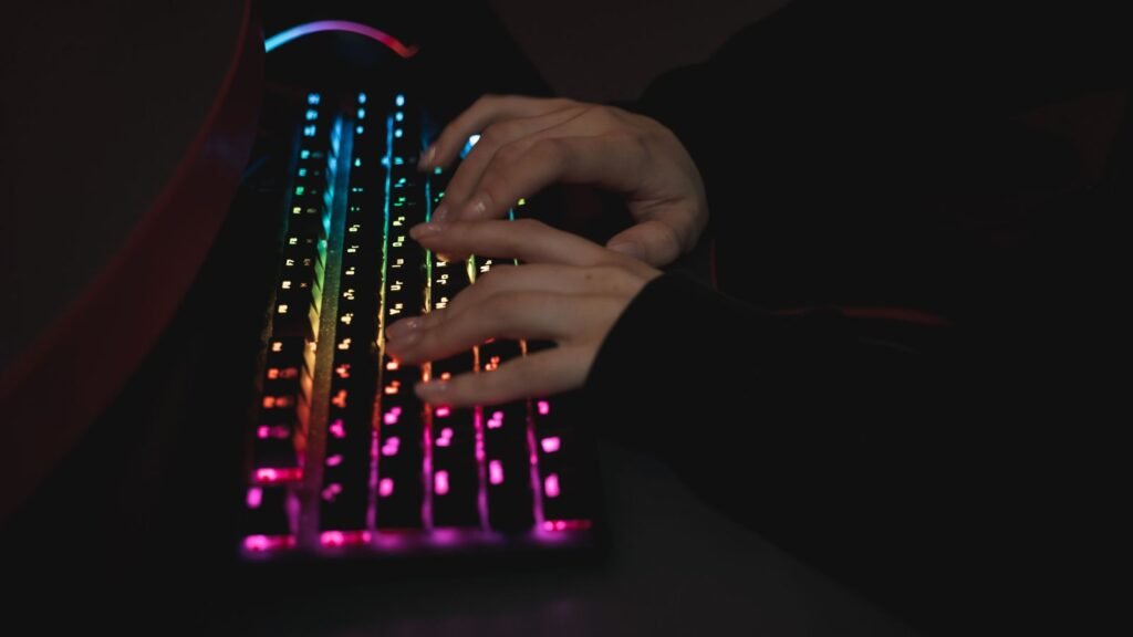 Hands typing on a dark keyboard with rainbow RGB backlighting