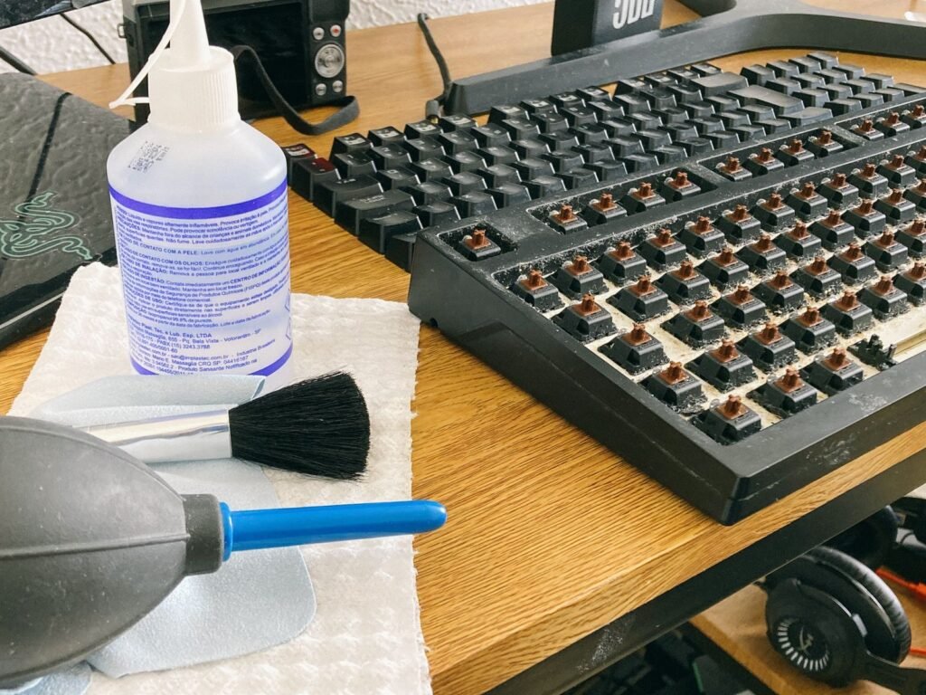 Isopropyl alcohol, a soft brush and an air blower next to a mechanical keyboard with its keycaps removed